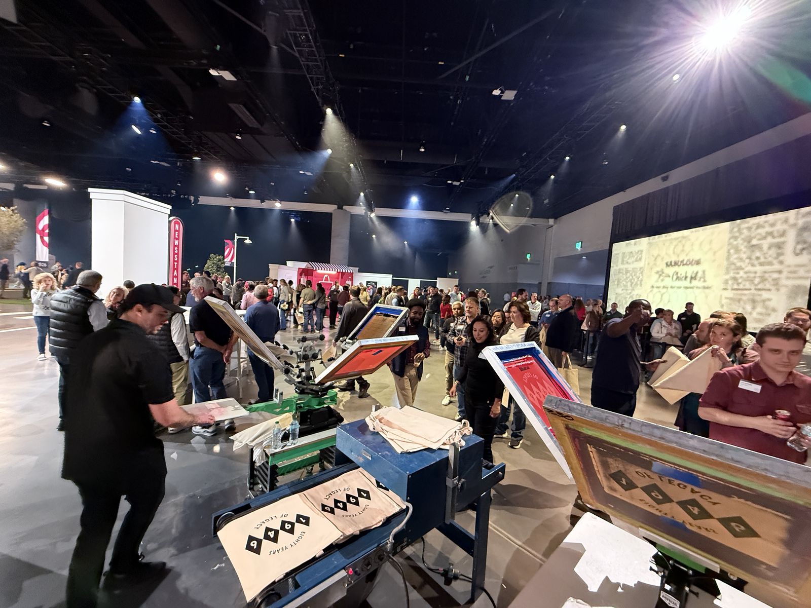 Custom merch stations mid-rush on an arena floor during a national franchise anniversary