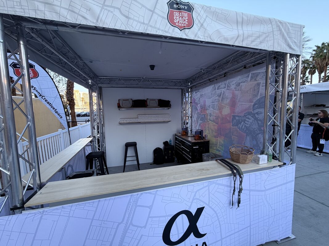 Truss-framed festival booth with counters and stools set up outdoors before gates open