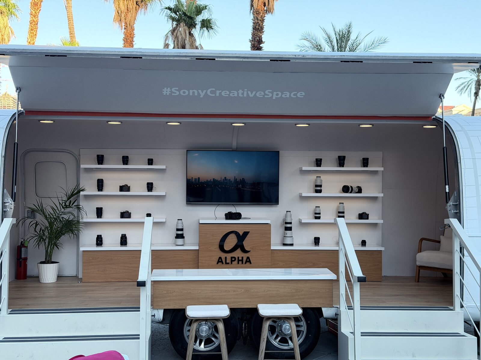 Open-sided brand trailer activation with product shelving under palm trees
