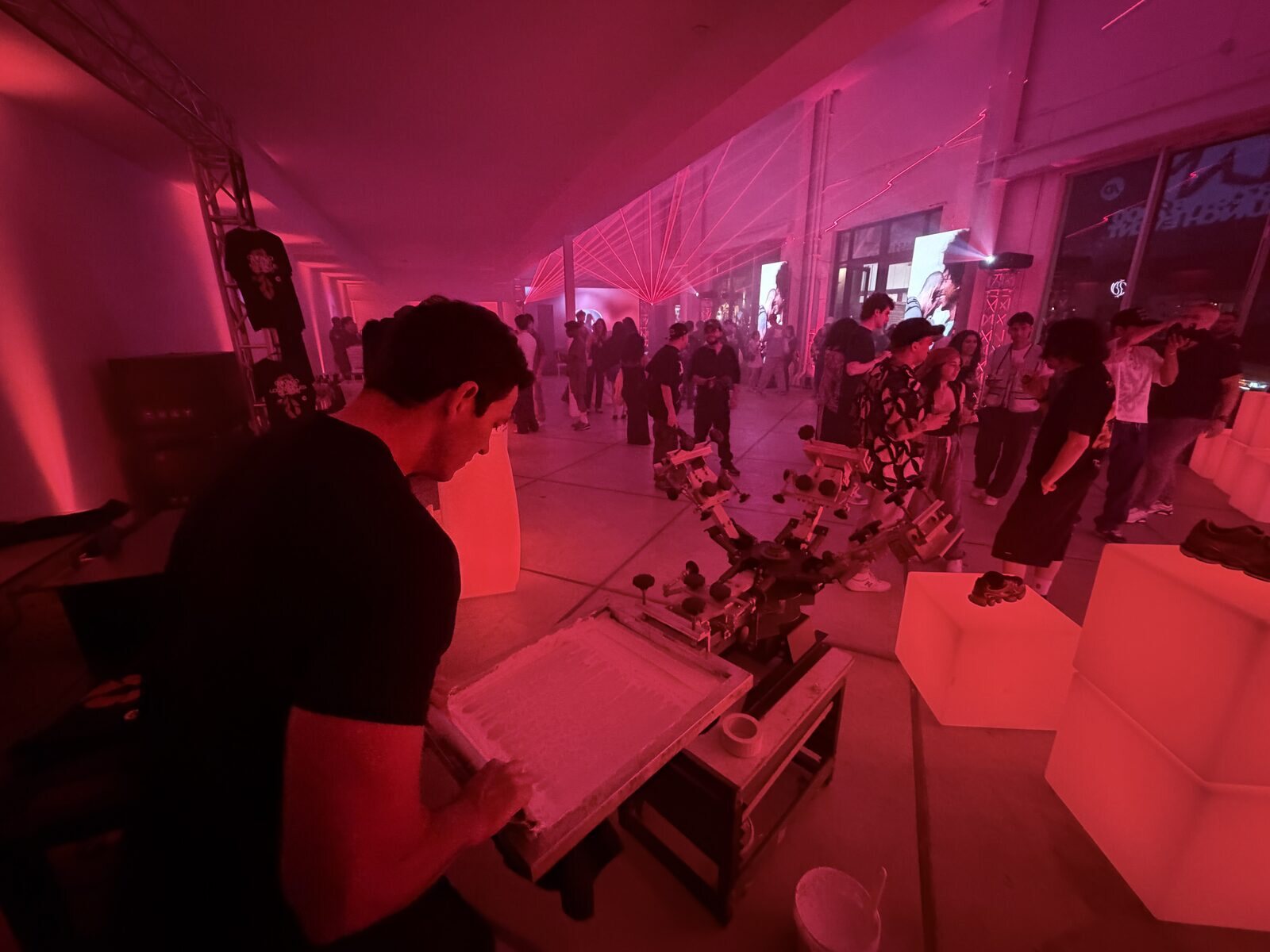 Live merch station under red lasers at a warehouse product launch afterparty